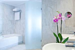 Badezimmer im Kontokali Bay Resort & Spa mit Badewanne, Waschbecken und Orchideenstrauß.