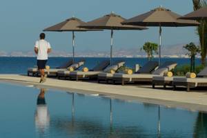 Mann im weißen T-Shirt und schwarzen Shorts geht am Pool des Kempinski Hotels Muscat entlang, neben Sonnenliegen und Sonnenschirmen.