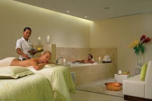 Massagebehandlung im Hotel Dreams Las Mareas Costa Rica mit einer Frau auf einer Liege und einem Mann im Whirlpool.