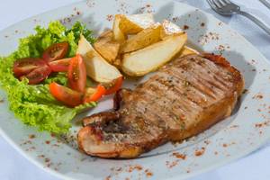 Gegrilltes Steak mit Gemüse und Kartoffel auf einem weißen Teller.