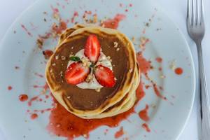 Ein Dessertteller mit zwei Stapeln von Pfannkuchen, überzogen mit Erdbeeren, Sahne und Beerensauce.