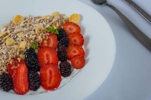 Ein weißer Teller mit Müsli, frischen Früchten und Kokosflocken.