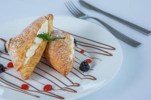 Zwei Croissants mit Sahne und Beeren auf einem weißen Teller mit Schokoladensauce und Minzblatt.