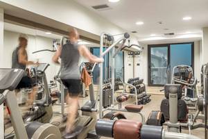 Fitnessstudio im Mitsis Rodos Village Beach Hotel mit verschiedenen Geräten und zwei Personen, die Cardiogeräte benutzen.