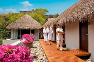 Gäste des Secrets Papagayo Costa Rica Hotel gehen auf einem Holzweg vorbei an Hütten.