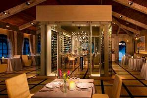 Innenbereich des Restaurants im Secrets Papagayo Costa Rica mit mehreren Tischen und Stühlen, einer großen Glaswand, Weinregal und dekorativen Lampen.