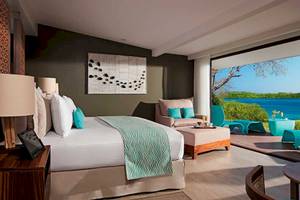Suite-Zimmer mit Meerblick im Secrets Papagayo Costa Rica mit einem großen Bett, Kissen, Lampen und einem großen Fenster mit Blick auf das Meer.