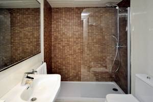 Badezimmer mit braunen Fliesen, Dusche, Spiegel und Toilette im Sol Wave House All Suites Hotel