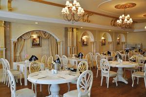Das elegante Restaurant des Nirvana Dolce Vita Hotels mit weißen Tischen und Stühlen, Kronleuchtern und dekorativen Wandbildern.