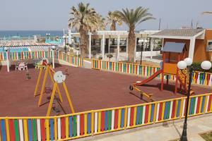 Kinderspielplatz im Freien im Europa Beach Hotel & Spa mit bunten Spielgeräten und Meer im Hintergrund.