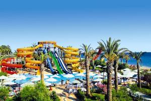 Wasserpark des Long Beach Alanya Hotels mit mehreren Rutschen und vielen Sonnenschirmen.