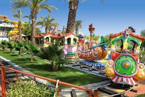 Kinderzug im Freizeitpark des Long Beach Alanya Hotels mit bunten Waggons und Palmen im Hintergrund.