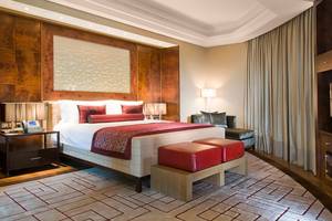 Schlafzimmer im Grand Millennium Al Wahda Hotel mit einem großen Bett, rotem Kopfteil und zwei Hockern.