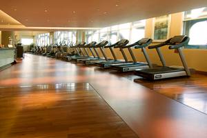Fitnessstudio im Grand Millennium Al Wahda Hotel mit mehreren Laufbändern und hellen Holzböden.