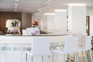Barbereich im Alua Leo Hotel mit weißen Stühlen und einer Theke voller Flaschen.