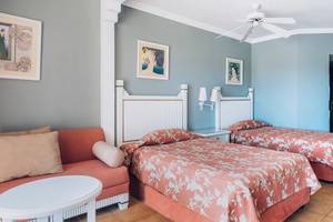 Doppelzimmer im Iberostar Laguna Azul Hotel mit zwei Betten, Couch, Nachttisch und Deckenventilator.