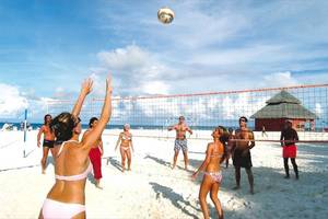 Gruppe von Leuten spielt Volleyball auf dem Strand mit einem Netz und einem Ball in der Luft.