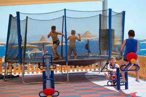 Kinder spielen auf einem Trampolin und anderen Spielgeräten am Strand, mit Blick auf das Meer.
