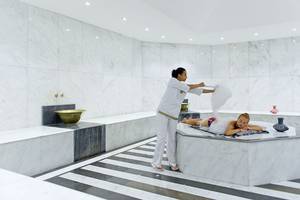 Eine Frau im weißen Outfit serviert einem Gast im Whirlpool im Spa-Bereich des Amphoras Beach Hotels.