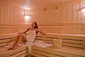 Eine Frau sitzt in einer Sauna des Amphoras Beach Hotels und hält einen Handtuch.