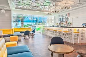 Innenansicht der Bar im H10 Las Palmeras Hotel mit Barkeeper, gelben Stühlen und modernem Design.