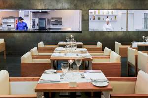 Innenansicht des Restaurants im H10 Las Palmeras Hotel mit gedeckten Tischen und Köchen, die im Hintergrund arbeiten.