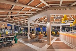 Innenbereich des H10 Las Palmeras Hotels mit Bar, Tischen und Stühlen, gelben Lampen und Holzboden.