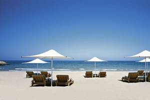 Strand mit Holzstühlen und Schirmen im Shangri-La Barr Al Jissah Resort