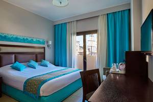 Hotelzimmer im Steigenberger Aqua Magic mit blauen Vorhängen, Doppelbett und Schreibtisch.