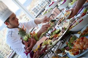 Koch beim Calypso Hotel bereitet ein Buffet auf einem Tisch mit verschiedenen Gerichten vor.