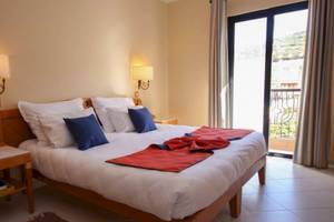 Schlafzimmer im Calypso Hotel mit einem Bett, Kissen und Decken, neben einem Fenster.