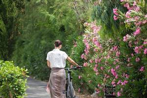 Frau mit Fahrrad am Cretan Malia Park entlang des Weges mit rosa Blumen
