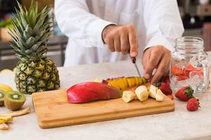 Person schneidet exotische Früchte wie Mango, Kiwi und Ananas auf einem Schneidebrett.