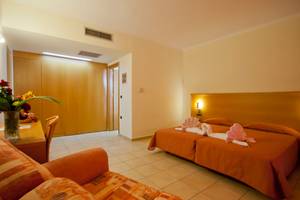Zimmer im Tigaki Beach Hotel mit zwei Betten und einer Couch, umgeben von Dekoration.