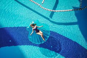 Eine Frau liegt entspannt auf einer Liege im blauen Pool des Alba Queen Hotels.