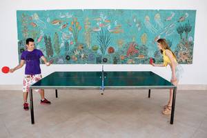 Ein Paar spielt Tischtennis vor einer Wand mit einem Wandteppich, der Meeresleben darstellt.