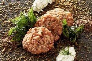 Fischkroketten von Myconian Kyma mit grünem Blattwerk und Gewürzen auf schwarzem Teller