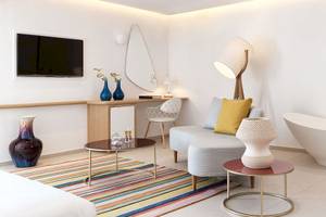 Innenansicht eines Zimmers im Myconian Kyma Hotel mit Badewanne, Fernseher, Couch und Tisch.