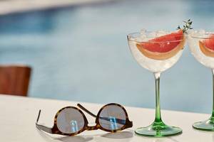 Zwei Gläser mit Gin und Tonic und einer Sonnenbrille auf einem Tisch am Pool