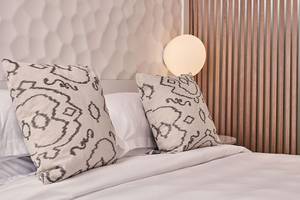 Bett im Myconian Kyma Hotel mit weißen Laken und gemusterten Kissen.