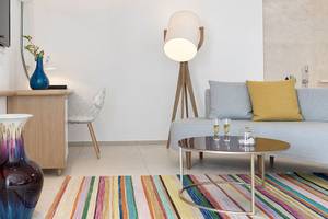 Inneneinrichtung des Myconian Kyma Hotelzimmers mit Schreibtisch, Stuhl, Fernseher, Lampe, Couch und Tisch.