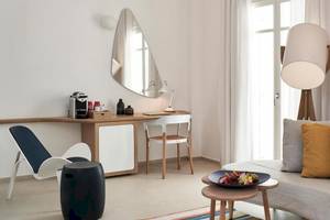 Zimmer im Myconian Kyma Hotel mit Schreibtisch, Stuhl, Lampe, Couch und offenem Buch.