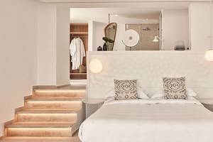 Schlafzimmer im Myconian Kyma Hotel mit Bett, Kissen, Nachttischen und beleuchteten Wandleuchten.