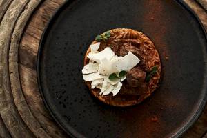 Ein Gericht auf einer schwarzen Holzplatte im Myconian Kyma Hotel, bestehend aus Fleischbällchen, Risotto und Käse.