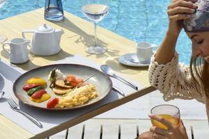 Frau genießt Frühstück am Pool im Myconian Kyma Hotel