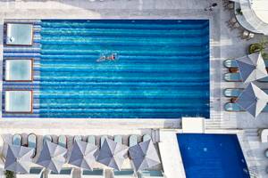 Luftaufnahme des Schwimmbeckens im Myconian Kyma Hotel mit Sonnenliegen und Sonnenschirmen