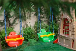 Zwei bunte Schaukeln und ein Spielhaus im Garten des Well Palace Side Hotels.
