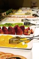 Buffet mit verschiedenen Obstsalaten und Früchten wie Erdbeeren, Kiwis und Orangen.
