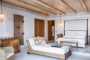 Schlafzimmer im Mitsis Blue Domes Resort mit weißem Bett, Nachttisch, Hängelampen und Wanddekor.