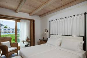 Schlafzimmer im Mitsis Blue Domes Resort & Spa mit weißem Bett, Nachttisch und Blick auf die Außenterrasse.